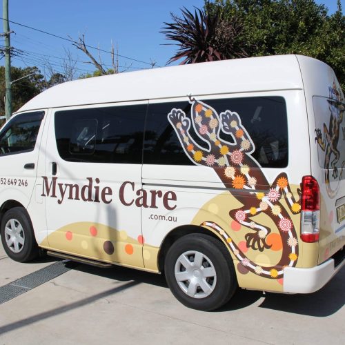 A Disability support service bus parked in front of some trees.