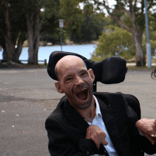 A man in a wheelchair is standing next to his disability support worker.