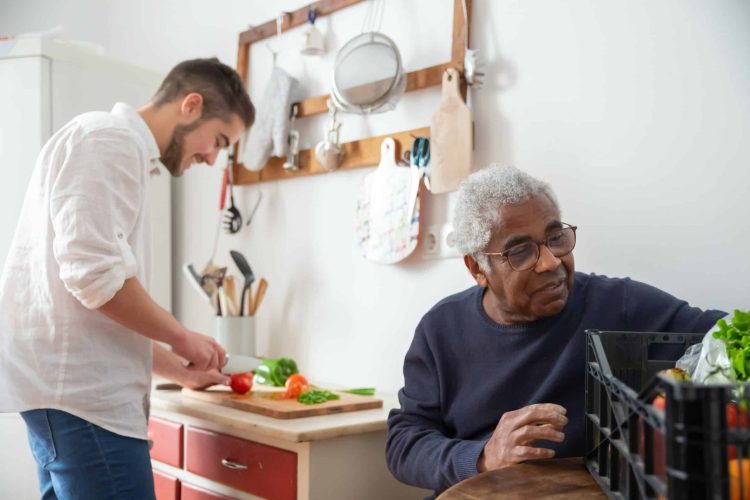 a young man is helping an elderly man by meal preparing for him